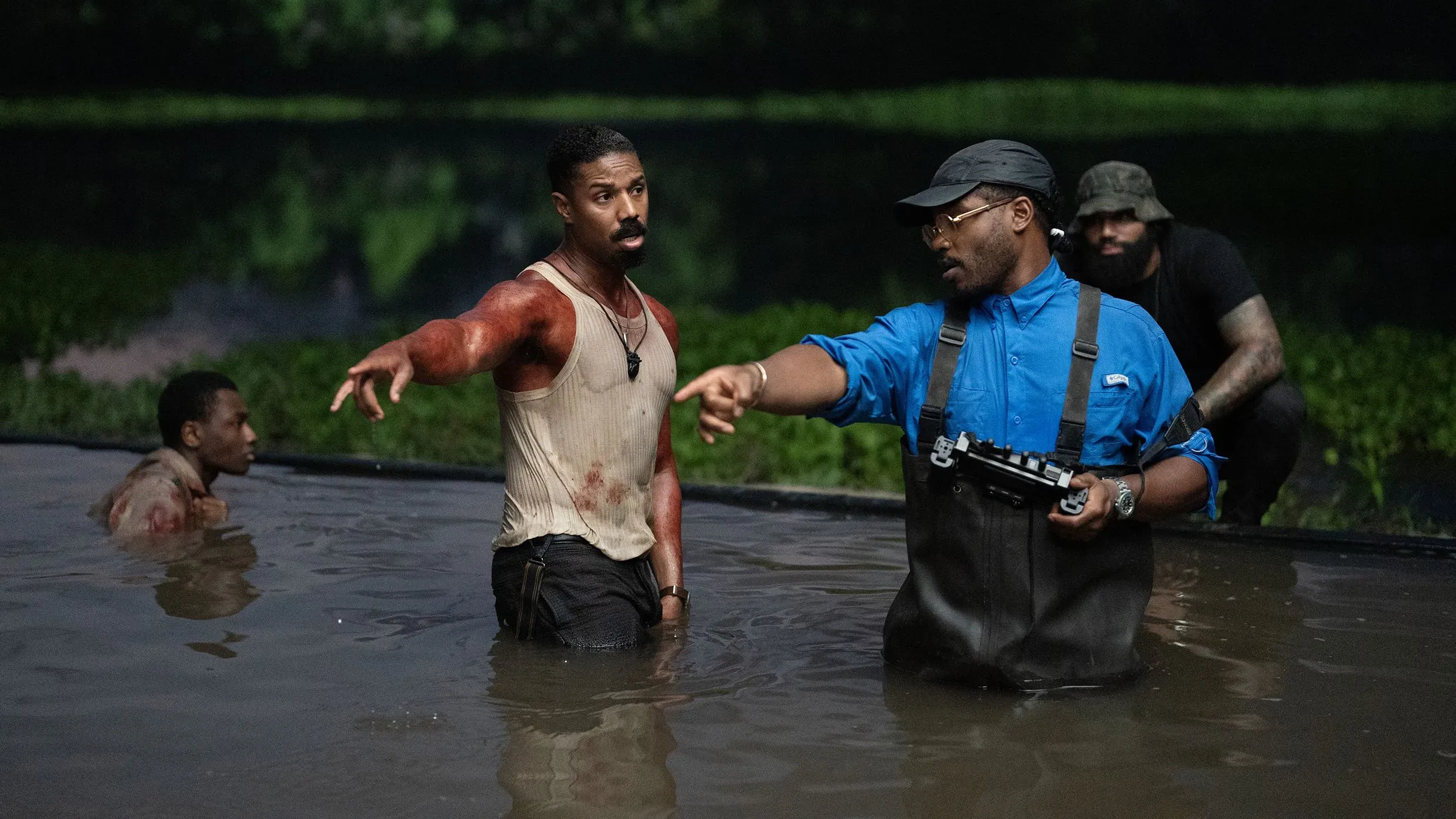 مشهد من فيلم "المذنبون" يظهر المخرج ريان كوجلر يتحدث مع الممثل مايكل ب. جوردان في مياه ضحلة، أثناء تصوير مشهد مثير.