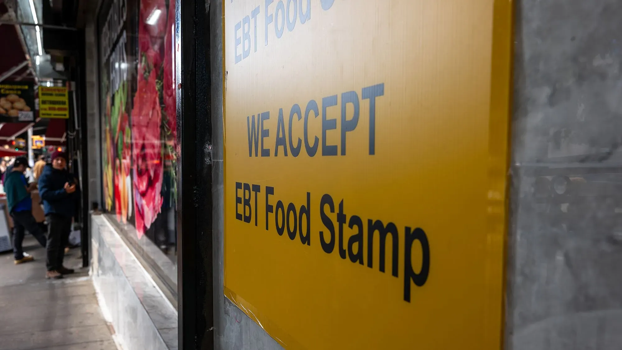 لافتة صفراء مكتوب عليها "نقبل طوابع الطعام EBT" في متجر، مع وجود أشخاص في الخلفية، تعكس تغييرات مقترحة في برنامج المساعدة الغذائية.