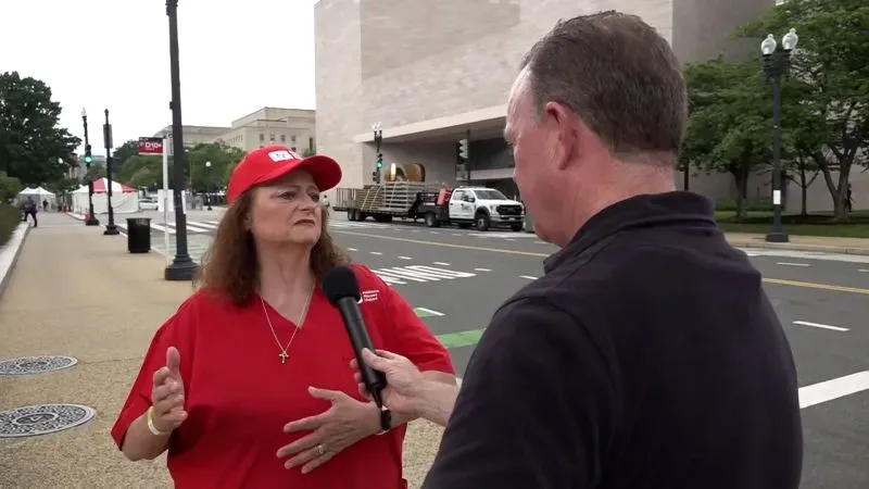 امرأة ترتدي قبعة حمراء تتحدث مع رجل يحمل ميكروفونًا في الشارع، تعبر عن مخاوفها بشأن تخفيضات وزارة شؤون المحاربين القدامى.