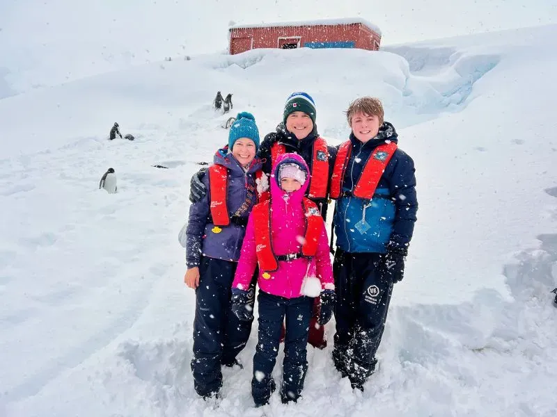 عائلة ألموند تتوسط الثلوج في القارة القطبية الجنوبية، مرتدين سترات النجاة، مع خلفية من المناظر الطبيعية الجليدية.