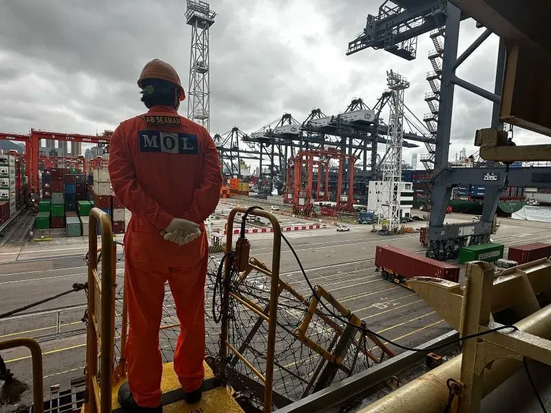 عامل في بدلة برتقالية يقف على متن السفينة "وان مودرن" في ميناء هونغ كونغ، بينما يتم تفريغ حاويات الشحن وسط أجواء غائمة.