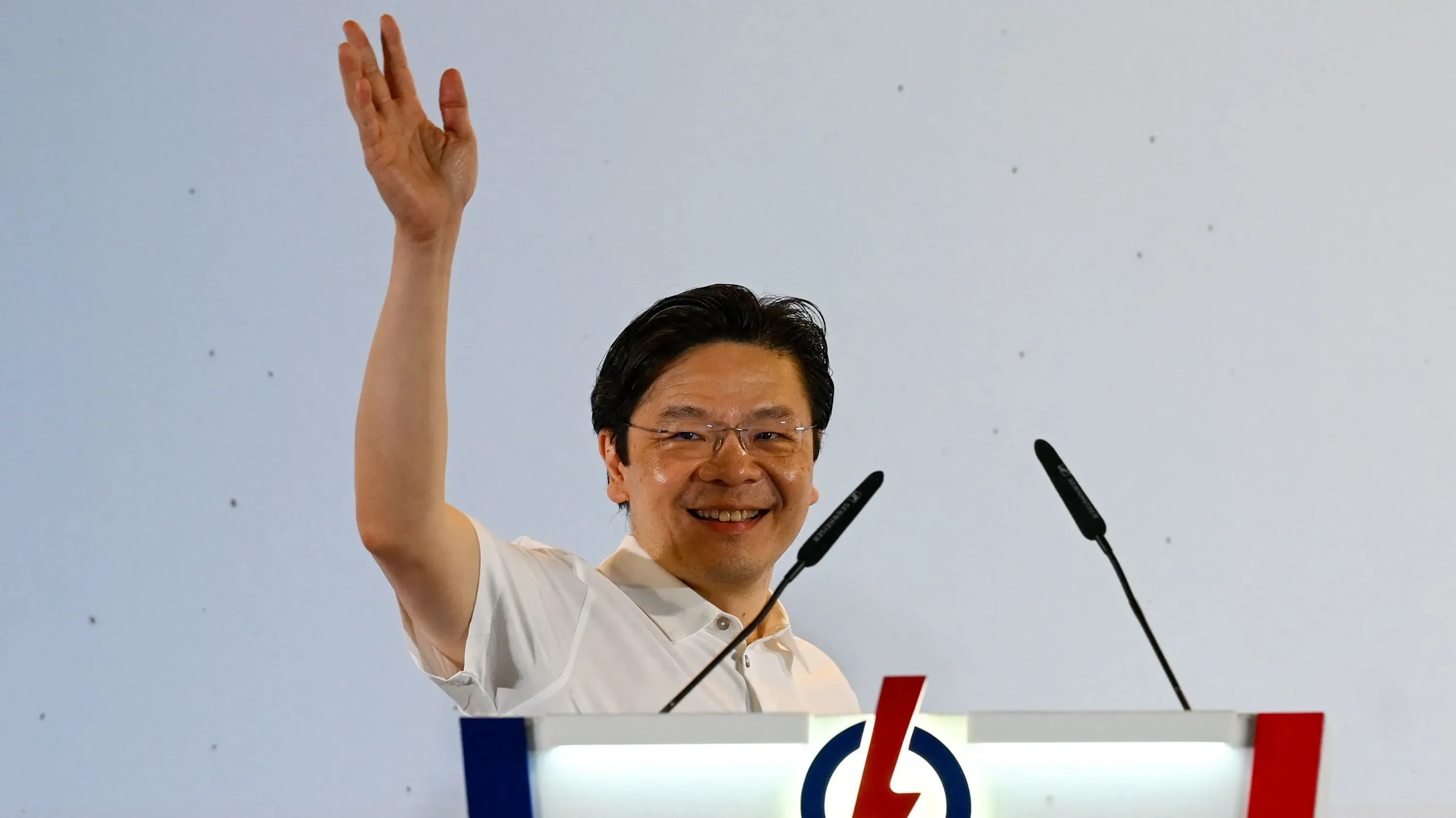 رئيس الوزراء لورانس وونغ يلوح بيده بعد فوز حزب العمل الشعبي في الانتخابات السنغافورية، مع خلفية بسيطة تبرز أجواء الاحتفال.