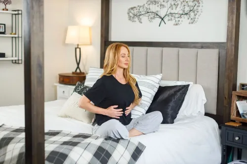 امرأة تجلس على السرير، تمارس التنفس الواعي بتركيز، مما يعزز الاسترخاء ويقلل من التوتر.