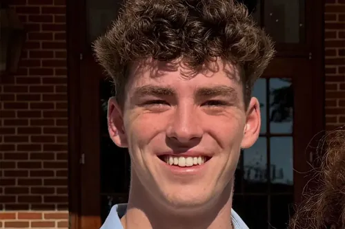 صورة لجيمس "جيمي" جرايسي، شاب أمريكي ذو شعر مجعد، مبتسم أمام مبنى، مع خلفية تظهر نوافذ خشبية.