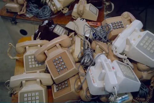 تجمع مجموعة من الهواتف الأرضية القديمة بألوان مختلفة، تعكس حقبة التسعينيات وتاريخ الاتصالات في الولايات المتحدة.
