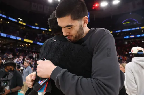 احتضان عاطفي بين لاعبين بعد انتهاء مباراة، مع جمهور خلفهم، يعكس مشاعر الفراق والتغيير في عالم الرياضة.