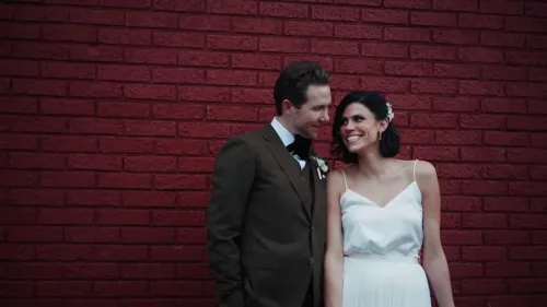 صورة لسبنسر ومونيك تيبي، زوجين مبتسمين في يوم زفافهما، يقفان أمام جدار أحمر. تعكس الصورة الحب والسعادة قبل مأساة مقتلهما.