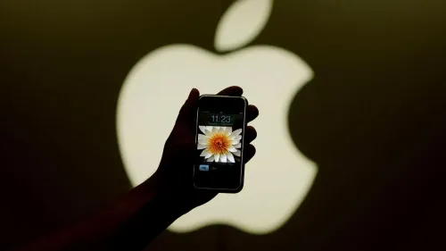 هاتف آيفون يظهر في يد شخص، مع شعار شركة آبل في الخلفية، مما يبرز أهمية الابتكار في عالم التكنولوجيا.