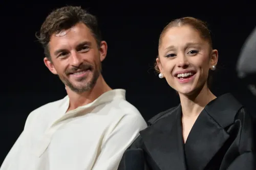 أريانا غراندي وجوناثان بيلي يبتسمان خلال حدث، مع خلفية داكنة، في إشارة إلى إحيائهما المسرحي "Sunday in the Park with George".