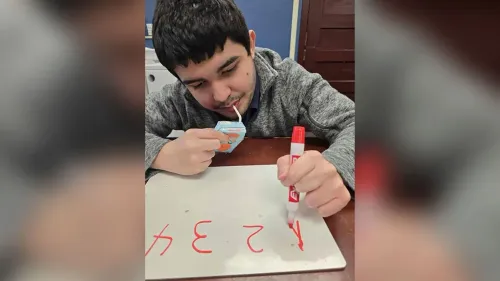 صبي مراهق يجلس على طاولة، يشرب من علبة عصير ويكتب على لوح أبيض بقلم أحمر، مع التركيز على ما يفعله.