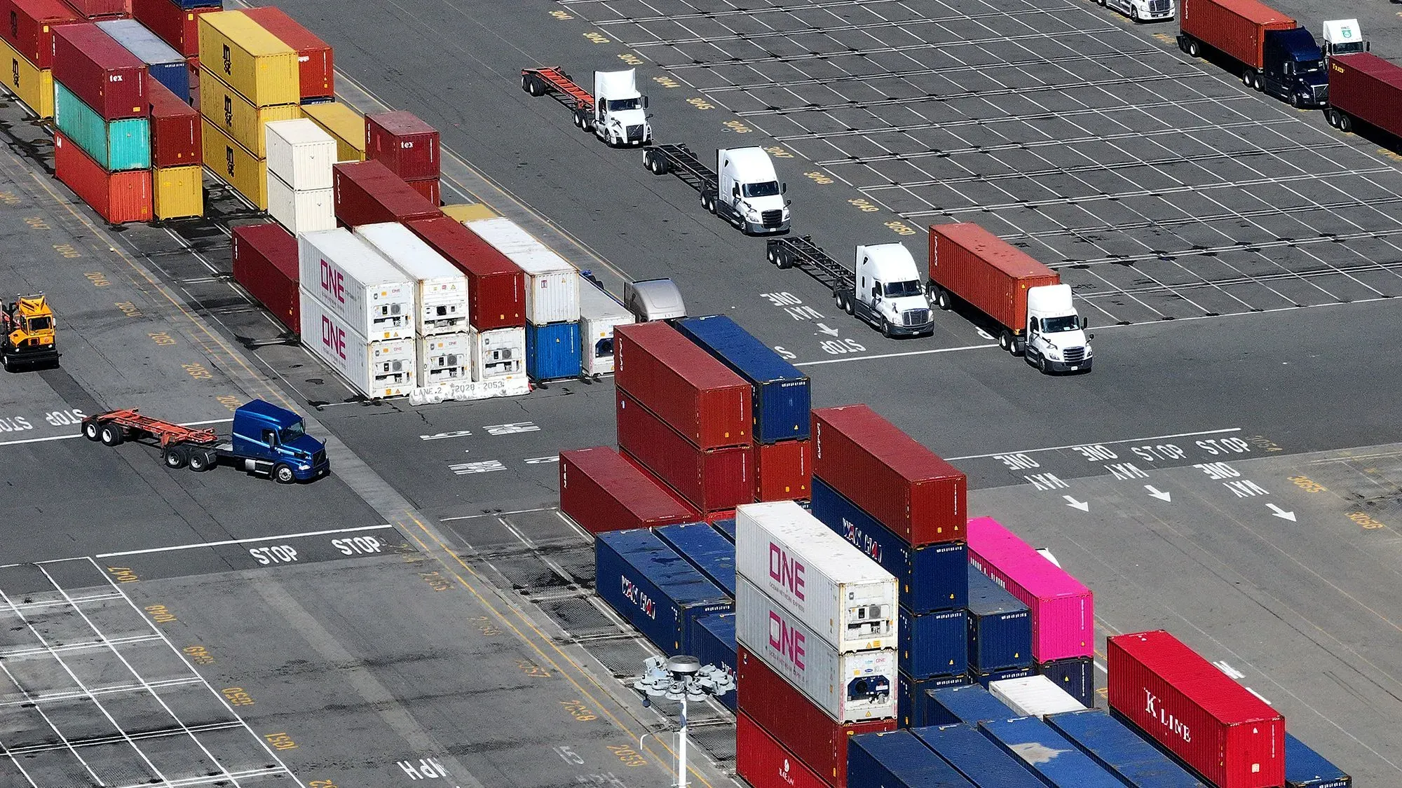 صورة لمرسى شحن يحتوي على حاويات ملونة وشاحنات نقل، تعكس تأثير التعريفات الجمركية على سلاسل التوريد للشركات الصغيرة.