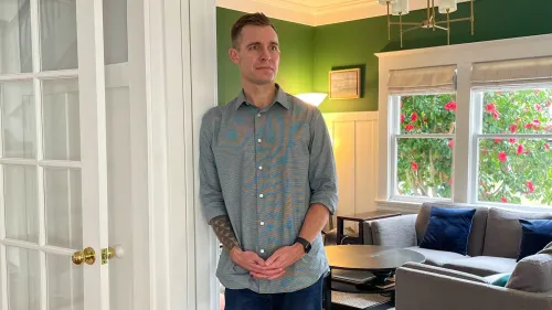 رجل يقف في غرفة معيشة ذات جدران خضراء، يبدو عليه التفكير. تعكس الصورة التوترات الأسرية حول توزيع الأعباء المنزلية.