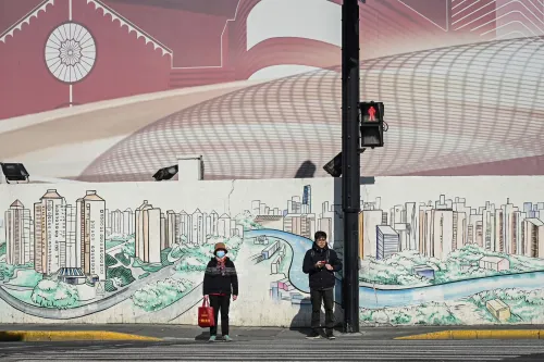 رجل وامرأة يقفان عند إشارة مرور أمام جدار مزخرف برسوم تعكس الحياة الحضرية في الصين، مما يعكس التحديات الديموغرافية الحالية.