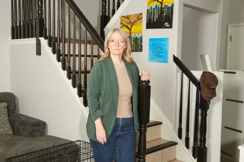 امرأة واقفة بجانب درابزين سلم في منزلها، تعبيرها يدل على القلق بسبب مشكلات في تقريرها الائتماني وتأثيرها على خططها المستقبلية.