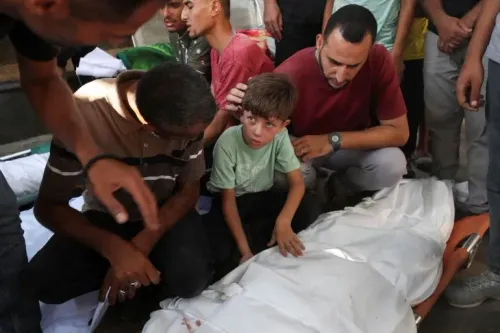 طفل صغير يبكي بجوار جثمان مغطى، محاط بأشخاص يعبرون عن حزنهم. تعكس الصورة معاناة المدنيين في غزة جراء الحرب.