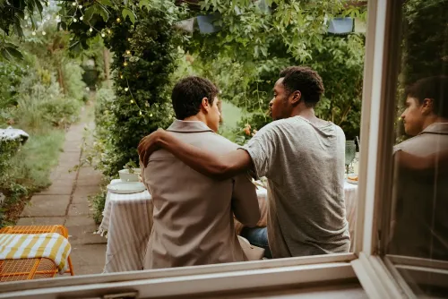 رجلان يجلسان معًا في حديقة، حيث يضع أحدهما يده على كتف الآخر. المشهد يعكس أهمية الروابط الاجتماعية والدعم المتبادل.