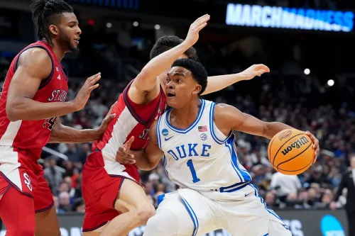 لاعب من فريق ديوك يتجاوز دفاع سانت جونز في مباراة بطولة NCAA، مع التركيز على الحركة الديناميكية للعبة.