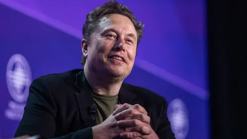 إيلون ماسك يتحدث في مؤتمر، مع تعبير واثق، محاط بأضواء خلفية ملونة، في سياق مناقشة مستقبل تسلا والتكنولوجيا الذاتية القيادة.