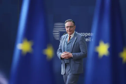 رجل يرتدي بدلة رسمية يقف أمام لافتة تحمل شعار الاتحاد الأوروبي، مع أعلام الاتحاد في الخلفية، في سياق مناقشات حول سياسة الطاقة.