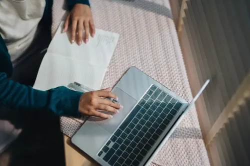 شخص يعمل على جهاز كمبيوتر محمول بينما يكتب في دفتر ملاحظات، مما يعكس التحديات التي يواجهها الشباب في العثور على وظائف.