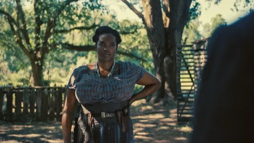 امرأة ترتدي ملابس تقليدية، تقف في بيئة خارجية، مع أشجار خلفها، تعبر عن قوة الشخصية في سياق فيلم "Color Purple".