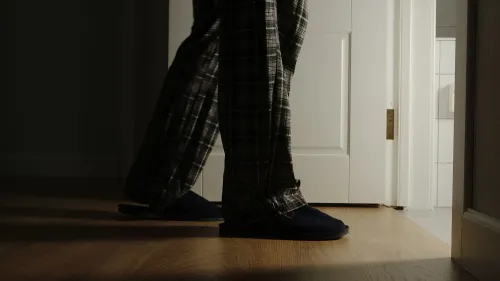 رجل يرتدي بيجاما يقف أمام باب الحمام في ظلام الليل، مما يعكس تجربة الاستيقاظ للتبول المتكرر.