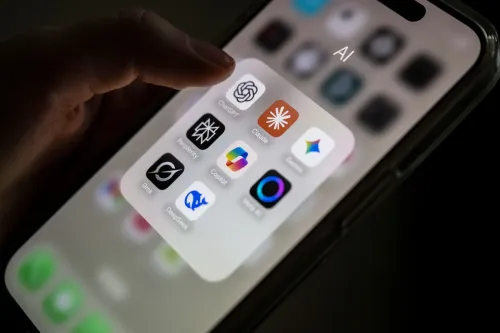 تظهر الصورة يدًا تمسك بهاتف ذكي يعرض مجموعة من تطبيقات الذكاء الاصطناعي، بما في ذلك ChatGPT وClaude، مما يعكس تأثير هذه التكنولوجيا على الحياة اليومية.