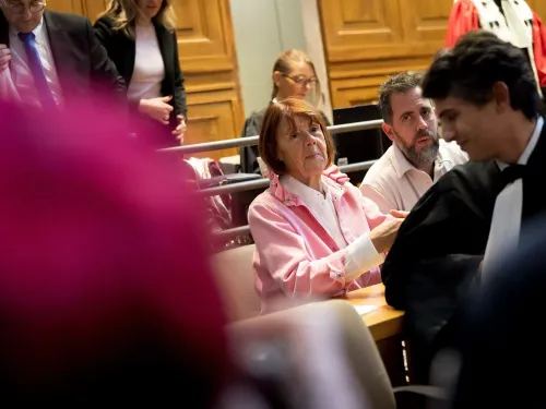 امرأة في قاعة المحكمة ترتدي سترة وردية، محاطة بمحامين ومشاهدين، تعكس أجواء محاكمة تتعلق بقضية اعتداء جنسي.