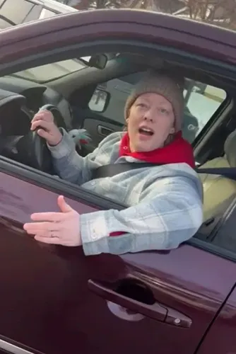 امرأة تجلس في سيارة، تتحدث وتبدو متفاجئة أو غاضبة، مع التركيز على تفاعلها أثناء عملية تتعلق بالهجرة.