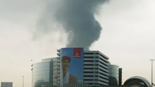 تصاعد الدخان من موقع حادث طائرة مسيرة بالقرب من مطار دبي، مع وجود لافتة لشركة طيران الإمارات في المقدمة.