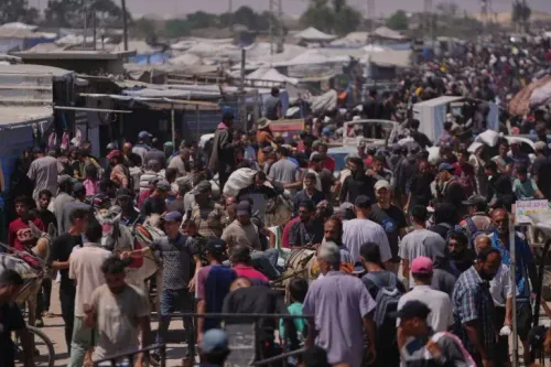 ازدحام كبير في منطقة تضم العديد من الفلسطينيين النازحين في رفح، مع وجود خيام ومركبات في الخلفية، يعكس الوضع الإنساني المتدهور.