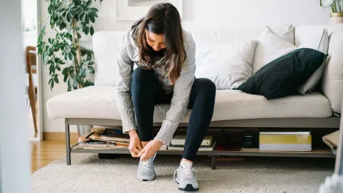 امرأة ترتدي حذاء رياضي في منزلها، مما يعكس أهمية الملابس في تعزيز الحافز والشعور بالتحسن.