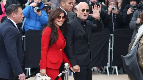 يظهر جيف بيزوس ولورين سانشيز بيزوس في عرض أزياء، حيث ترتدي سانشيز بدلة حمراء، بينما بيزوس يرتدي ملابس سوداء ونظارات شمسية.