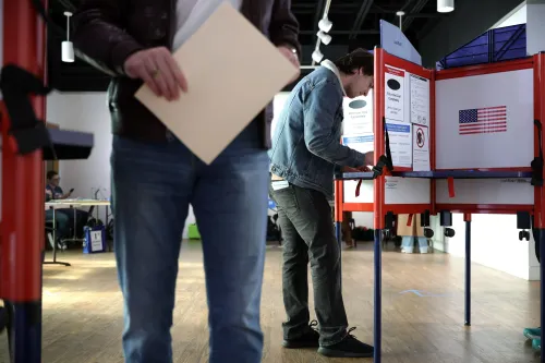 ناخب يقف أمام آلة التصويت في مركز اقتراع، حاملًا ورقة، بينما يظهر في الخلف أشخاص آخرون. تعكس الصورة أهمية التصويت في سياق النقاش حول قانون إنقاذ أمريكا.