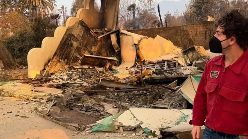 صورة تظهر حطام منزل مدمر بفعل حريق إيتون، مع وجود شخص يرتدي كمامة يتفقد الأضرار في موقع الحادث.