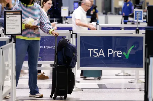ازدحام في مطار مع وجود لافتة تشير إلى "TSA Pre" بينما يسير مسافرون يحملون حقائبهم، مما يعكس تأثير الإغلاق الجزئي على السفر.