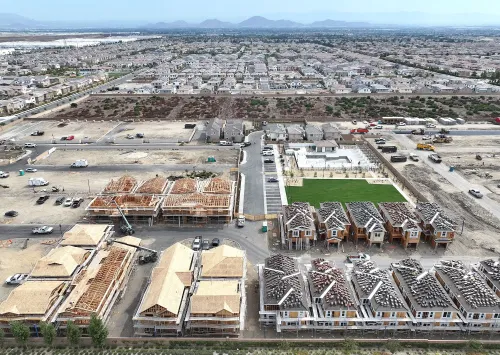 مشهد جوي لحي سكني قيد الإنشاء، يظهر منازل جديدة في مراحل مختلفة من البناء، مع مناظر طبيعية محيطة ومنازل قائمة في الخلفية.