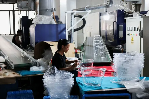 امرأة تعمل في مصنع لتصنيع المنتجات البلاستيكية، حيث تظهر آلات الإنتاج وأدوات التعبئة والتغليف، مما يعكس تأثير ارتفاع أسعار النفط على السوق.