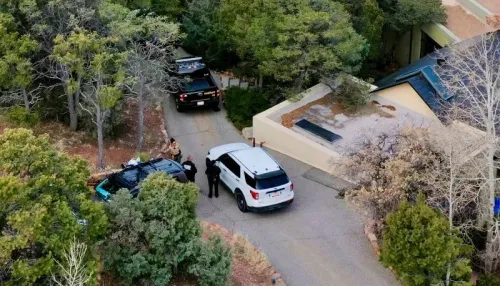 مشهد خارجي لمنزل جين هاكمان في سانتا في، يظهر سيارات الشرطة والأمن في الموقع وسط الأشجار، بعد التحقيق في وفاة الزوجين.