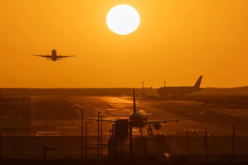 طائرة تقلع تحت شمس غاربة، مع طائرات أخرى متوقفة على المدرج، تعكس تأثير نقص وقود الطائرات على السفر الجوي.