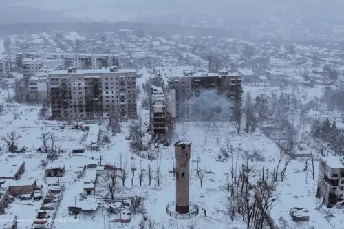 منظر لبلدة متضررة في أوكرانيا، تغطيها الثلوج، مع مباني مدمرة وأبراج مياه، تعكس آثار الصراع المستمر.