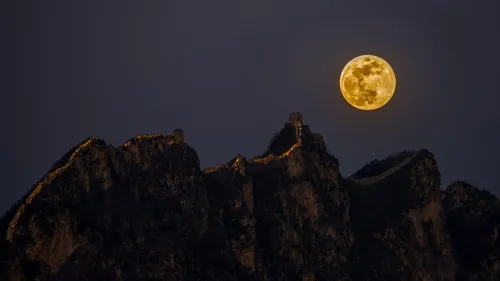 بدر فبراير يضيء السماء فوق الجبال، مع تفاصيل الجدار العظيم مرئية في الأسفل، مما يعكس جمال القمر في فترة الشتاء.