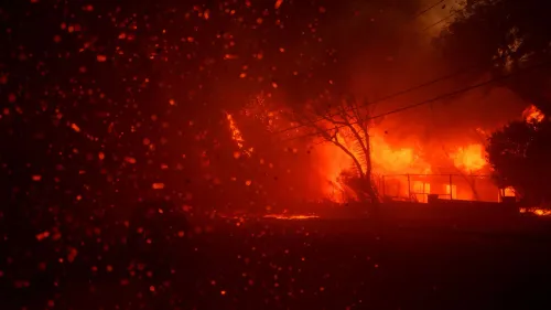 لهب ناري يلتهم الأشجار والمنازل في باسيفيك باليساديس، مع سحب من الدخان الكثيف، وسط أجواء مقلقة بسبب حرائق الغابات.