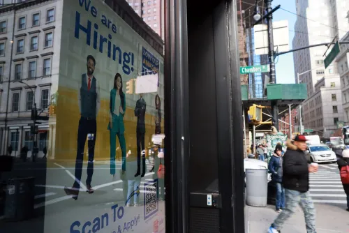 إعلان توظيف يعرض مجموعة من الأشخاص في ملابس رسمية، مع نص "نحن نوظف!"، في شارع مزدحم بمدينة نيويورك.