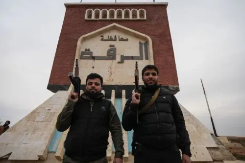 مقاتلان يحملان أسلحة يقفان أمام لافتة كبيرة مكتوبة عليها "محافظة الرقة"، في سياق السيطرة العسكرية للجيش السوري على المنطقة.