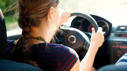 فتاة تقود السيارة بتركيز، تعكس تجربة المراهقين في تأجيل الحصول على رخصة القيادة بسبب الضغوط الاقتصادية والنفسية.