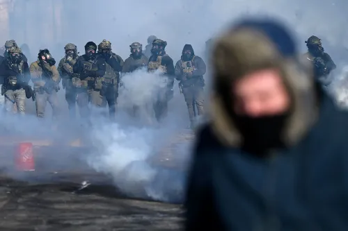 مواجهة بين قوات الأمن والمتظاهرين في منطقة ملبدة بالغيوم بالدخان، مع وجود أفراد يرتدون ملابس عسكرية وأقنعة واقية.