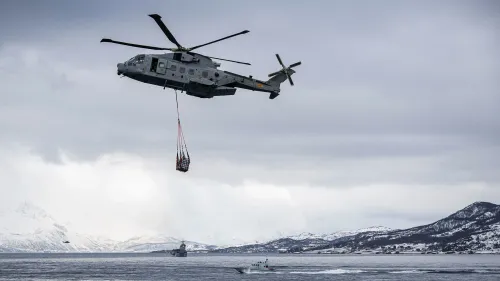 طائرة هليكوبتر عسكرية تحمل حمولات فوق منطقة قطبية، مع وجود سفينة في الأسفل وجبال مغطاة بالثلوج في الخلفية، تعكس التوترات العسكرية في القطب الشمالي.