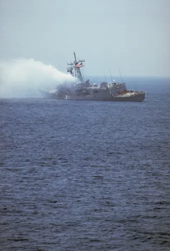 سفينة حربية أمريكية تتعرض لضرر كبير نتيجة هجوم صاروخي، مع تصاعد الدخان في البحر، مما يعكس التوترات في حرب الناقلات.