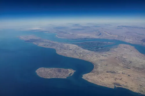 صورة جوية لمضيق هرمز، تُظهر الجزر المحيطة والمياه الزرقاء، مما يبرز أهميته كممر حيوي لنقل النفط العالمي.